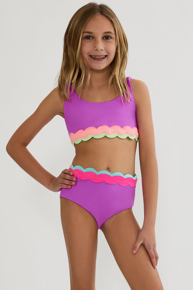 Young girl wearing a colorful two-piece swimsuit on a plain background