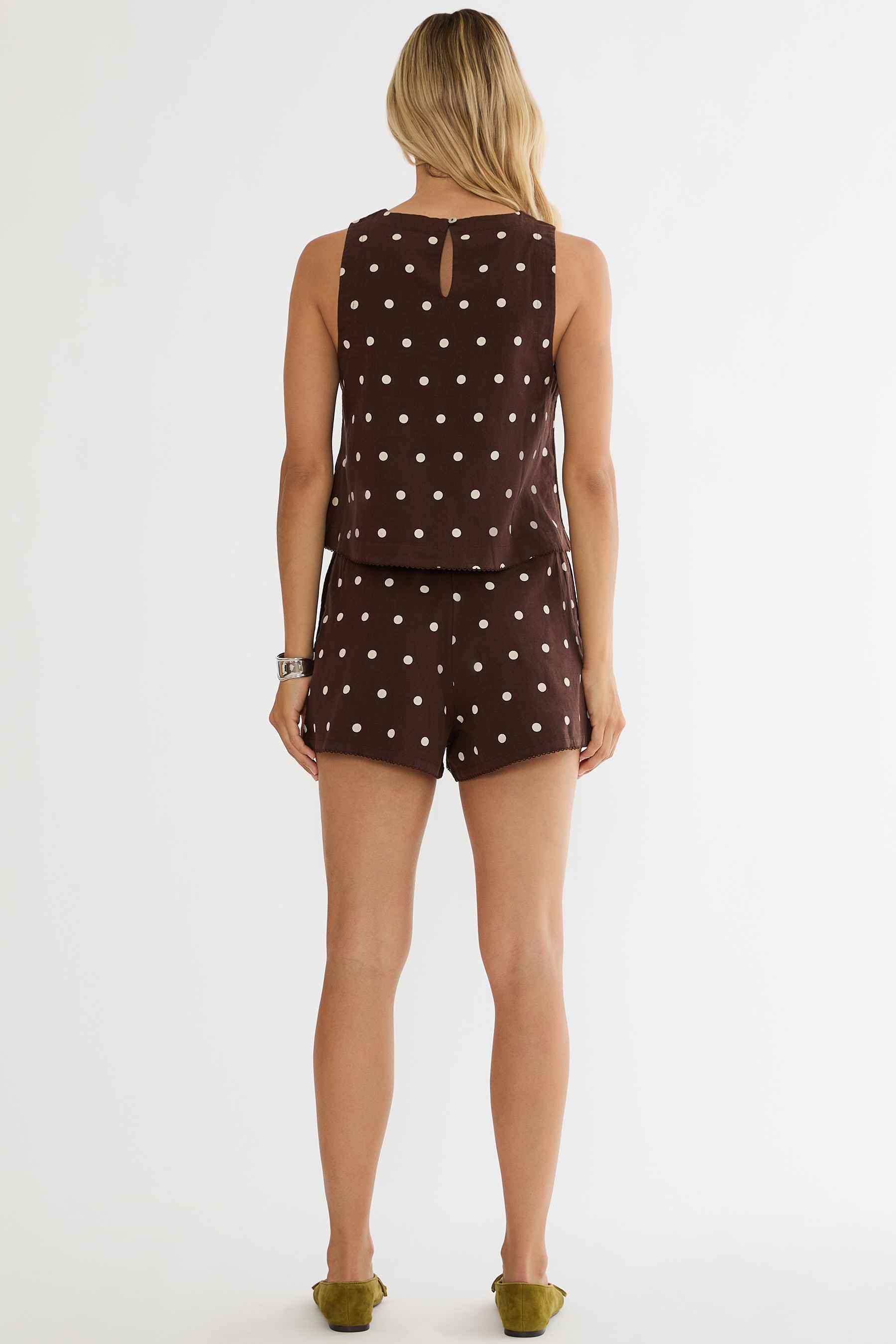 Woman wearing a brown polka dot sleeveless top and shorts on a white background