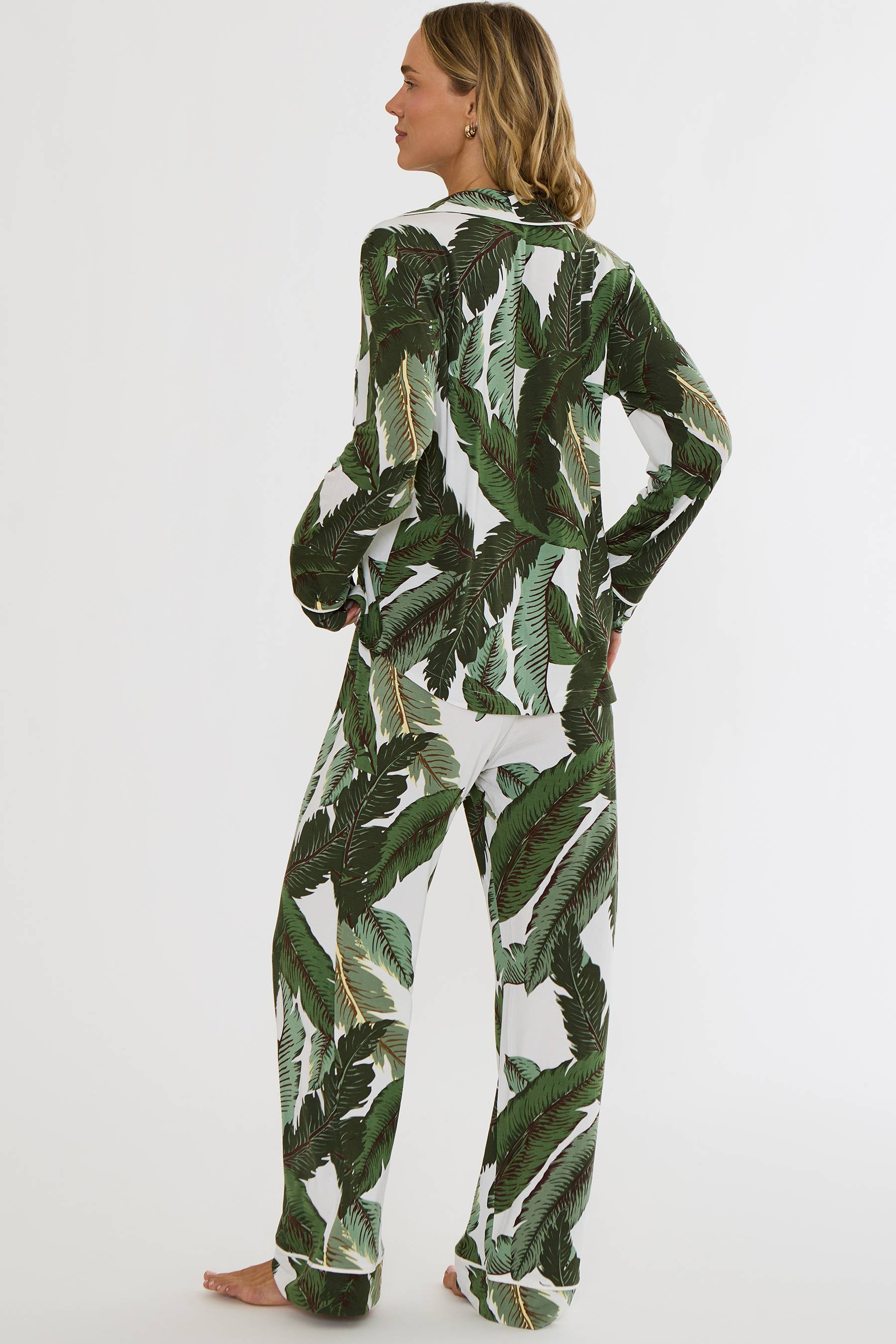 A woman modeling a matching two-piece pajama set with a green palm leaf print on a white background, shown from the back against a plain white studio backdrop.