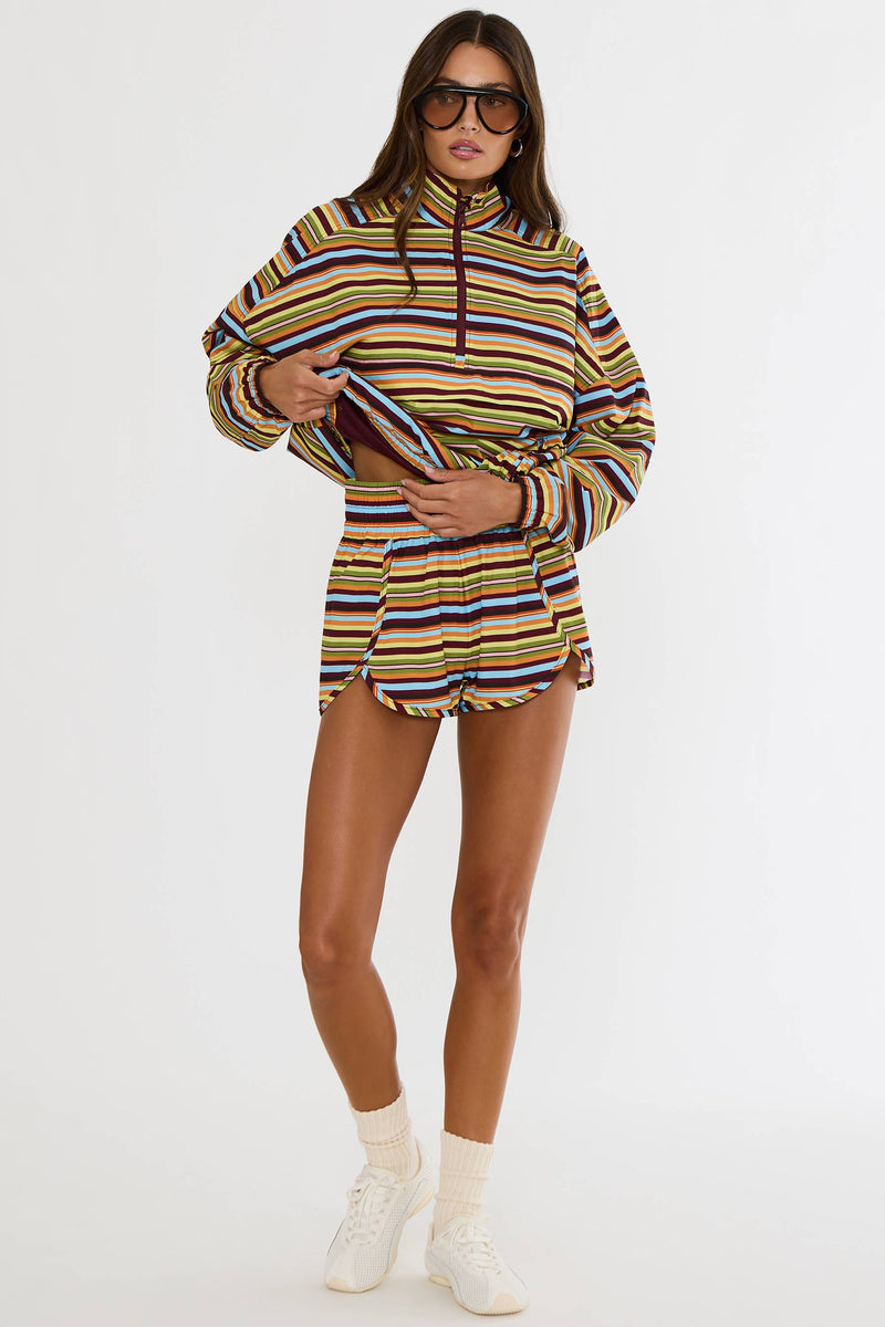 A model wearing a colorful striped zip-up hoodie and matching striped shorts, styled with white sneakers, white socks, and sunglasses against a plain white studio background.