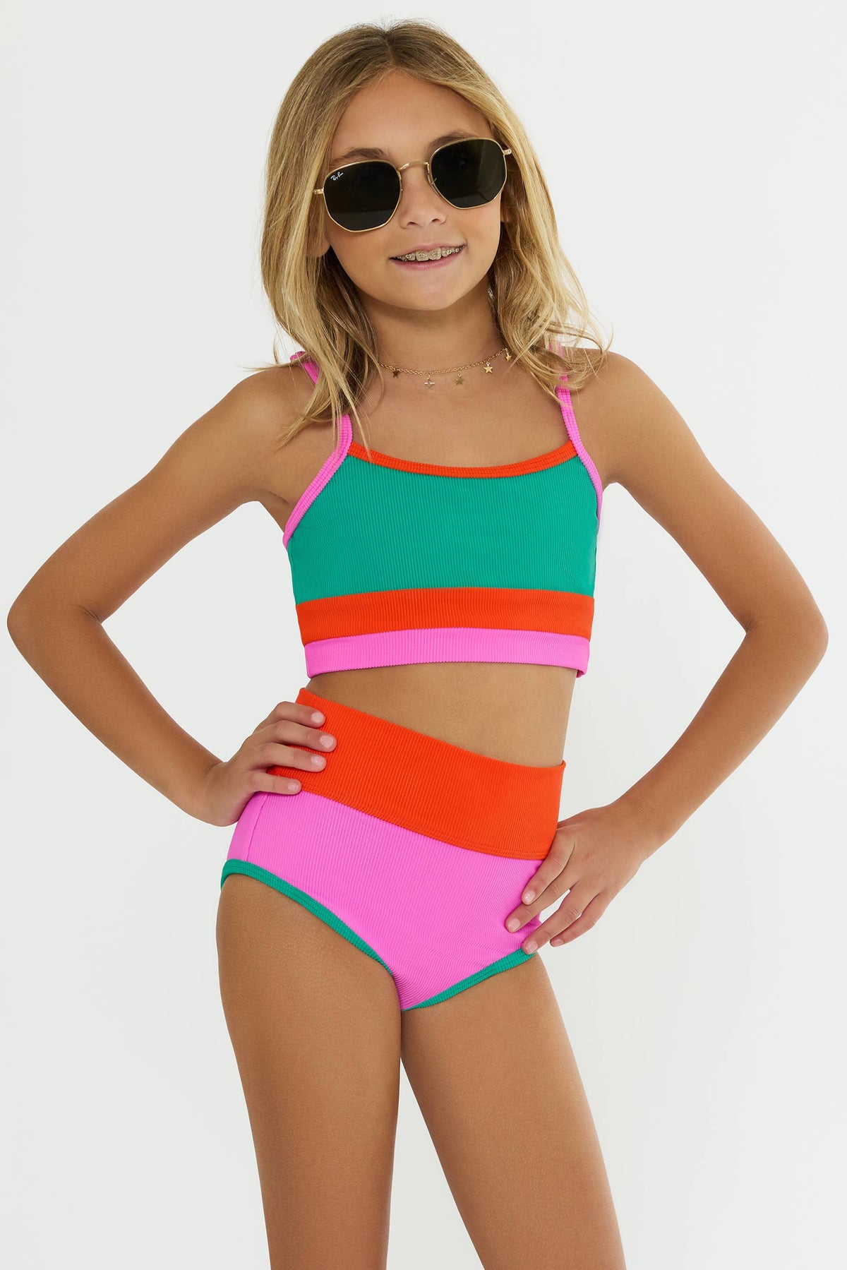 Little girl wearing a color block bikini in front of a white wall. 