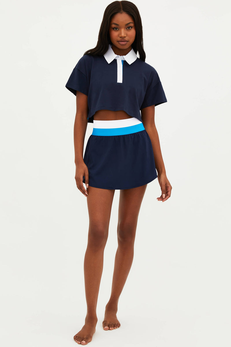 A model wearing a navy blue sports skirt with a built-in pair of shorts and a contrasting white collar.