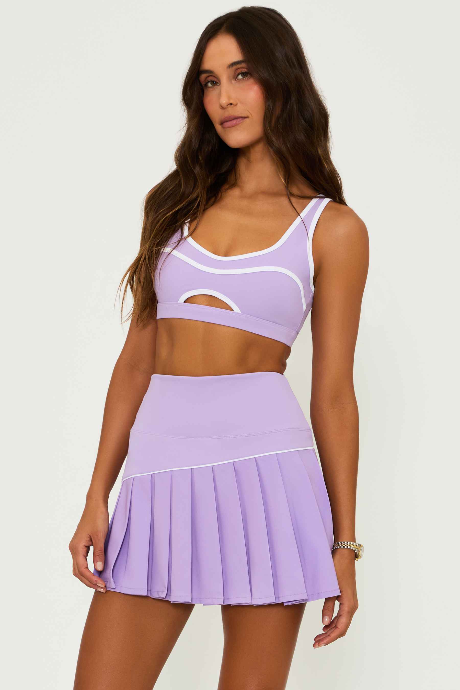 lavender pleated tennis skirt with a with contrast trim and a matching lavender sports bra with a cutout detail and white contrast trim