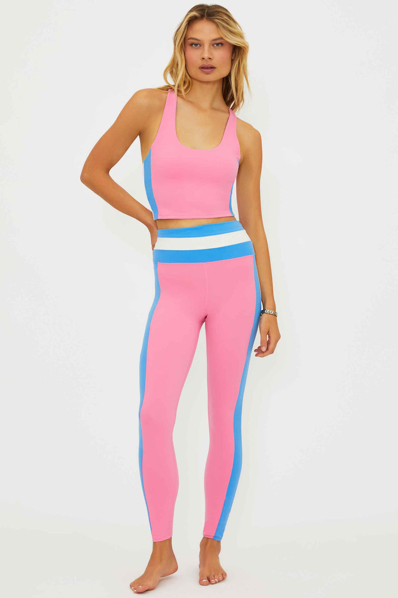 Woman wearing a pink sports bra and leggings with blue side panels on a white background