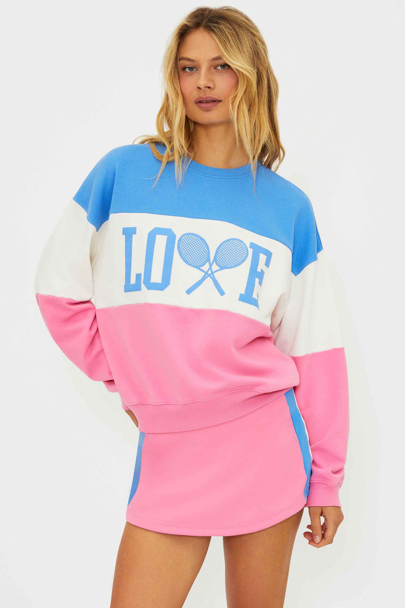Woman wearing a colorful 'LOVE' sweater with a tennis racket design on a white background