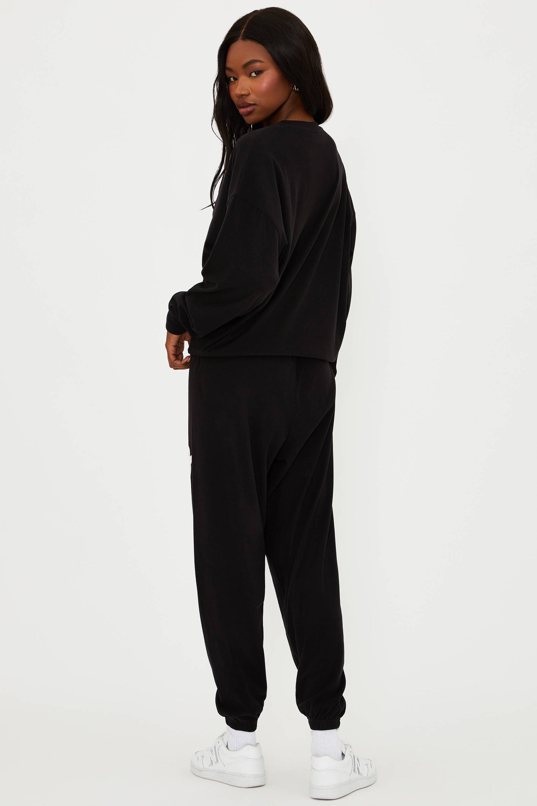 Person wearing a black tracksuit with white sneakers on a white background