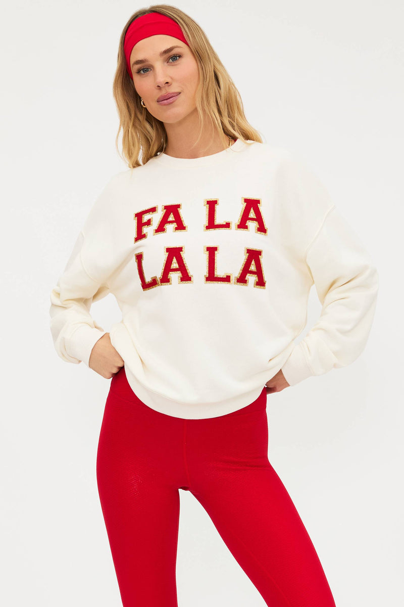 Woman wearing a cream sweatshirt with 'FA LA LA LA' text and red pants on a white background