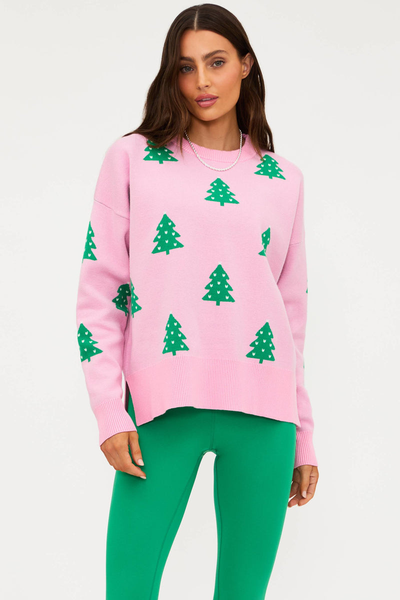 Woman wearing a pink sweater with green tree patterns and green pants on a white background