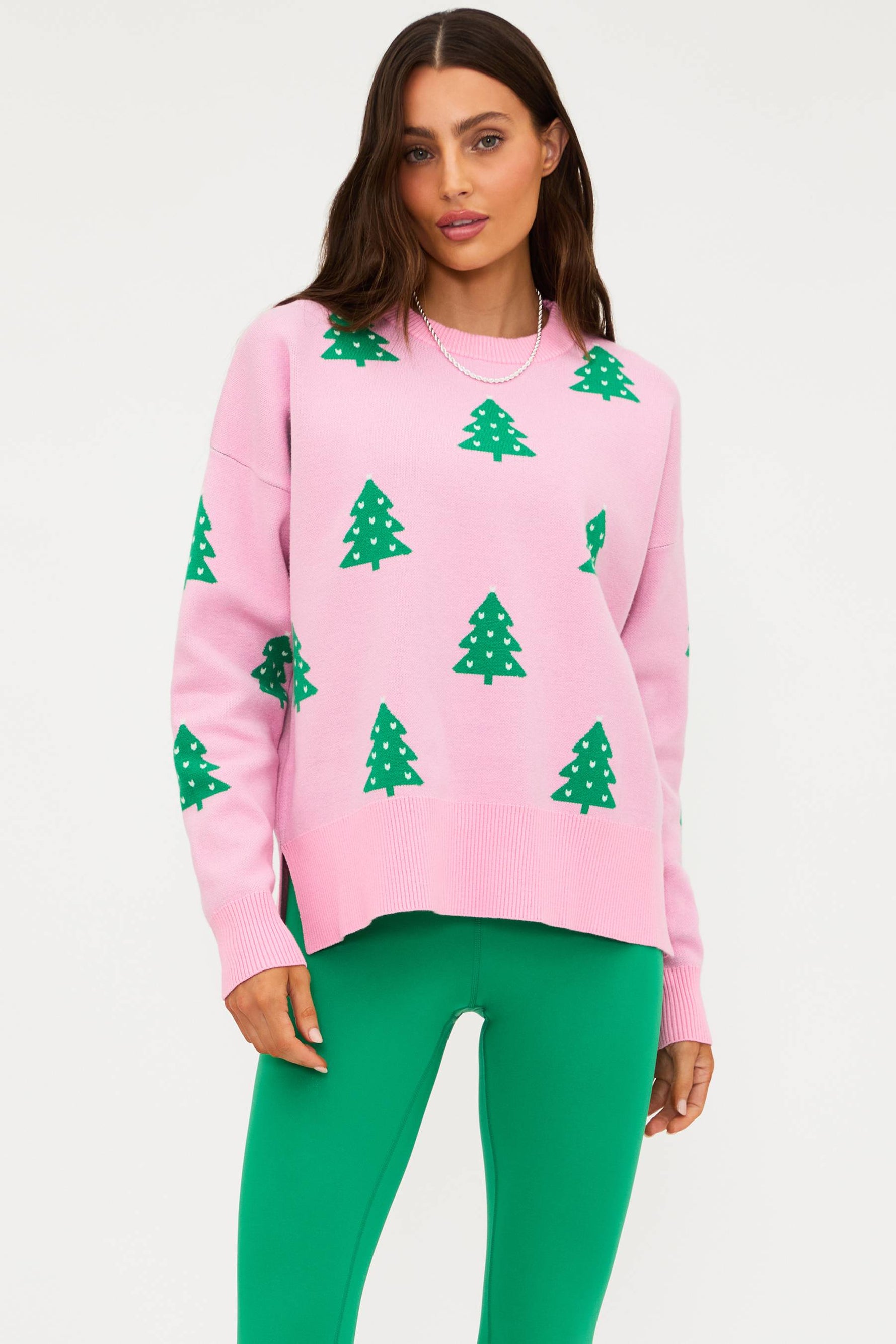 Woman wearing a pink sweater with green tree patterns and green pants on a white background