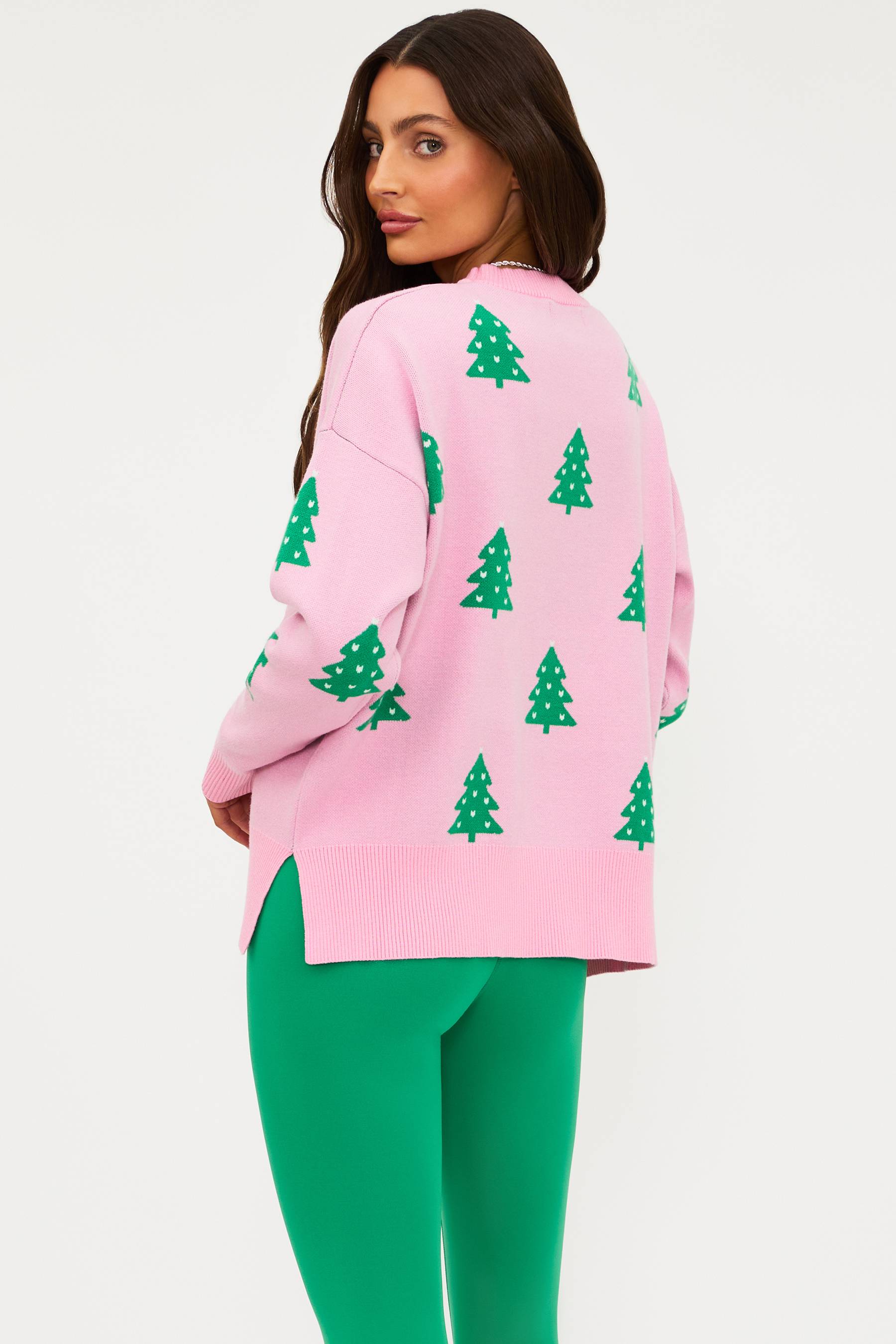 Woman wearing a pink sweater with green tree patterns and green pants on a white background