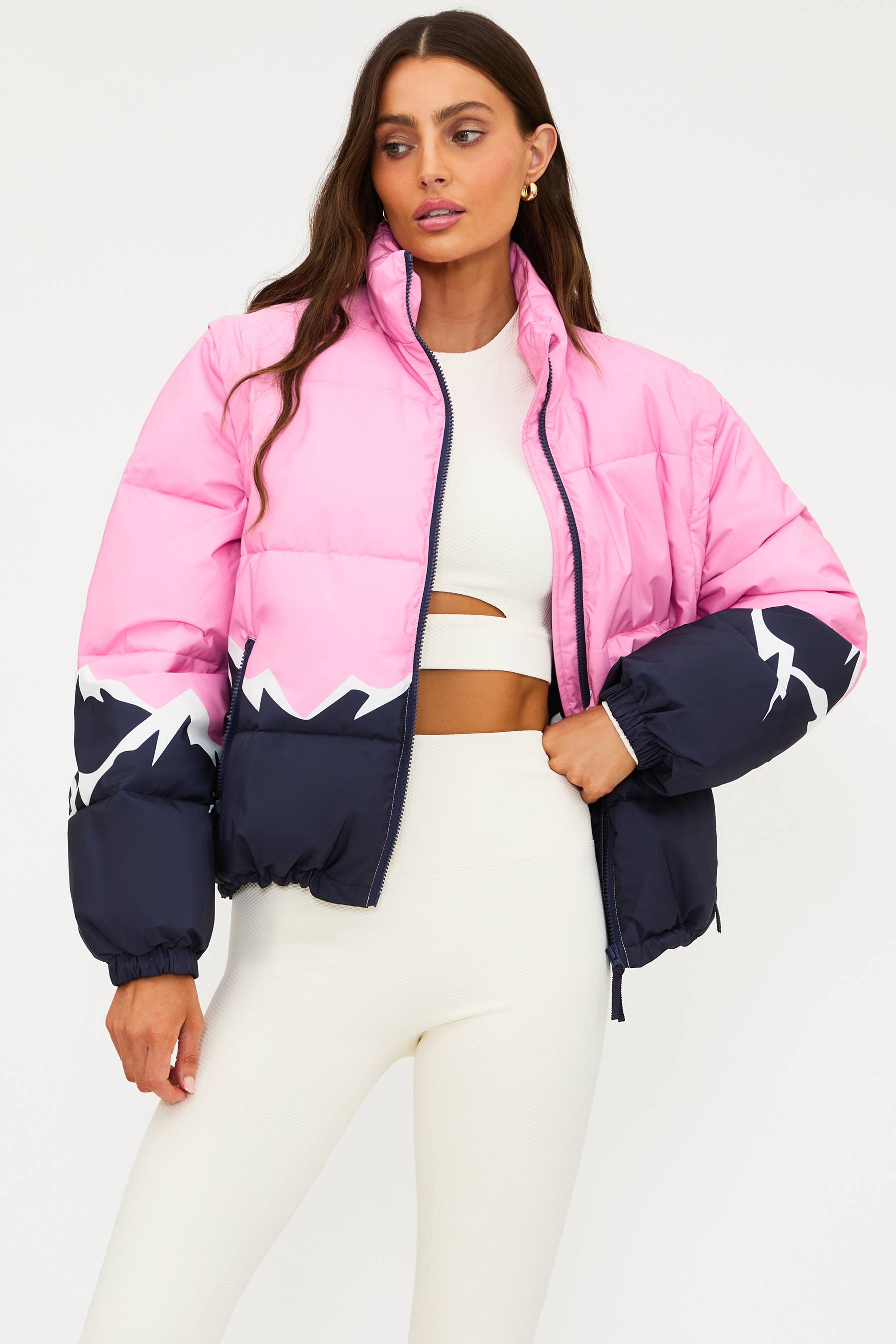 Woman wearing a pink and navy puffer jacket with white patterns on a white background