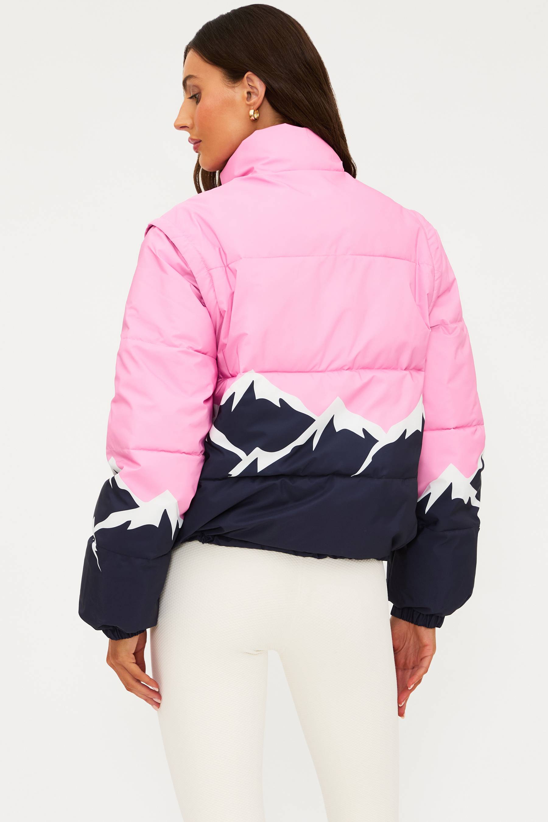 Woman wearing a pink and navy puffer jacket with white patterns on a white background