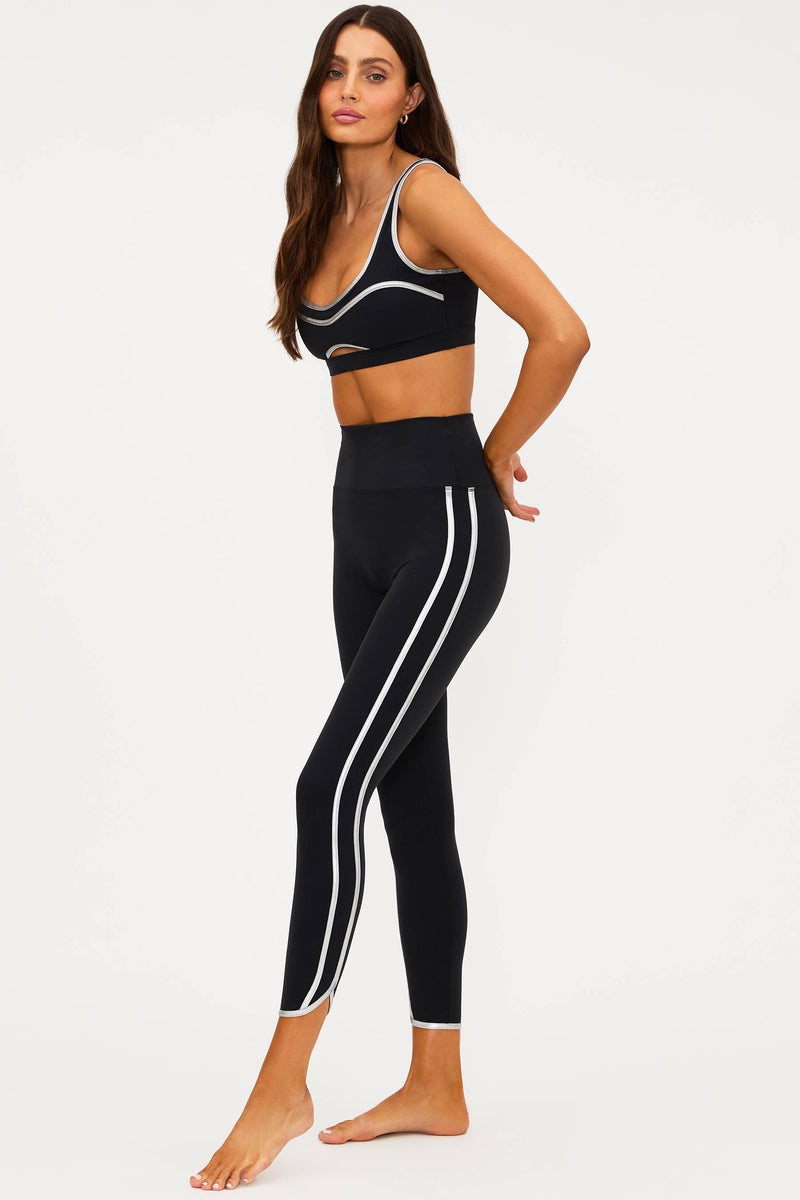 Woman wearing a black sports bra and leggings with white stripes on a white background