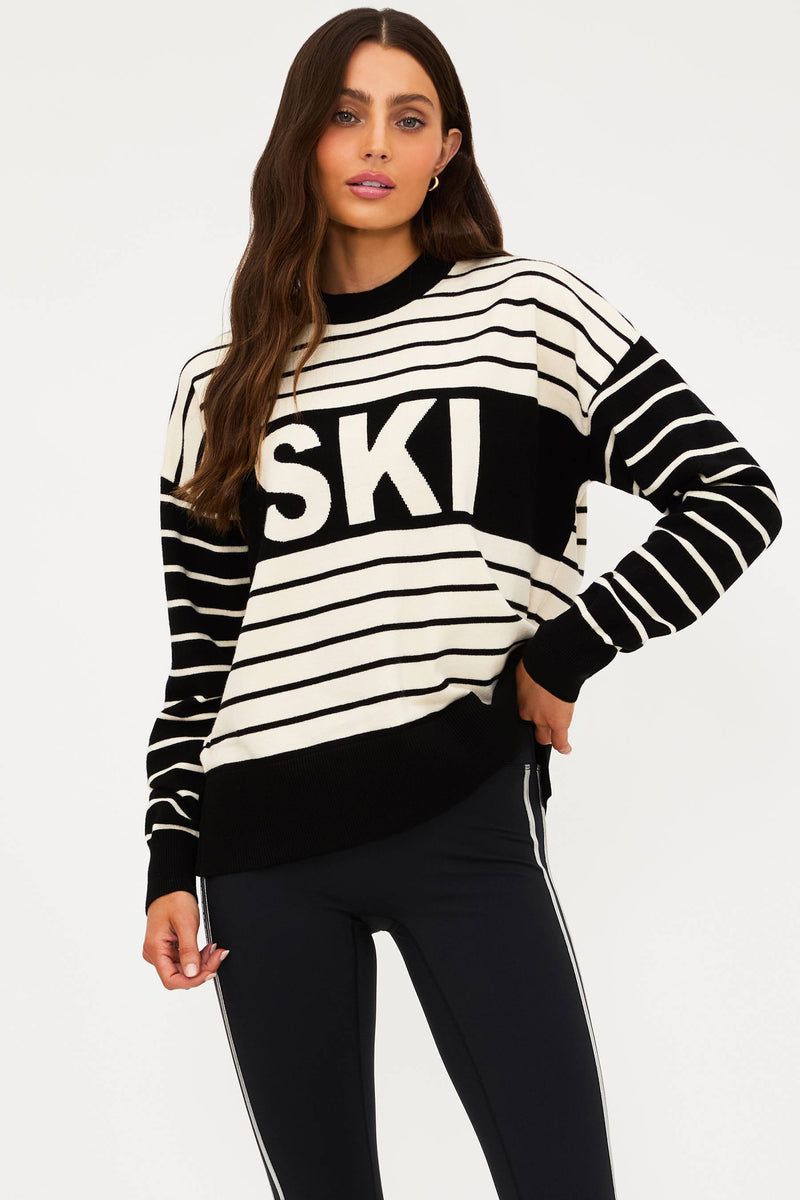 Woman wearing a black and white striped sweater with 'SKI' text on a plain background