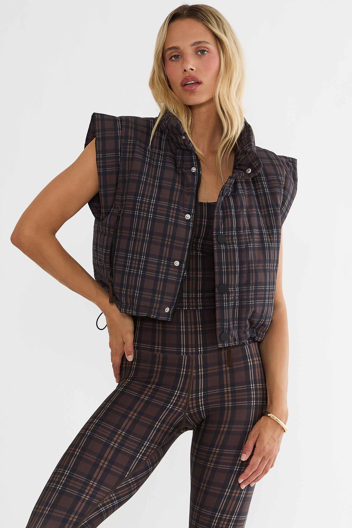 Woman wearing brown plaid cropped puffer vest. 