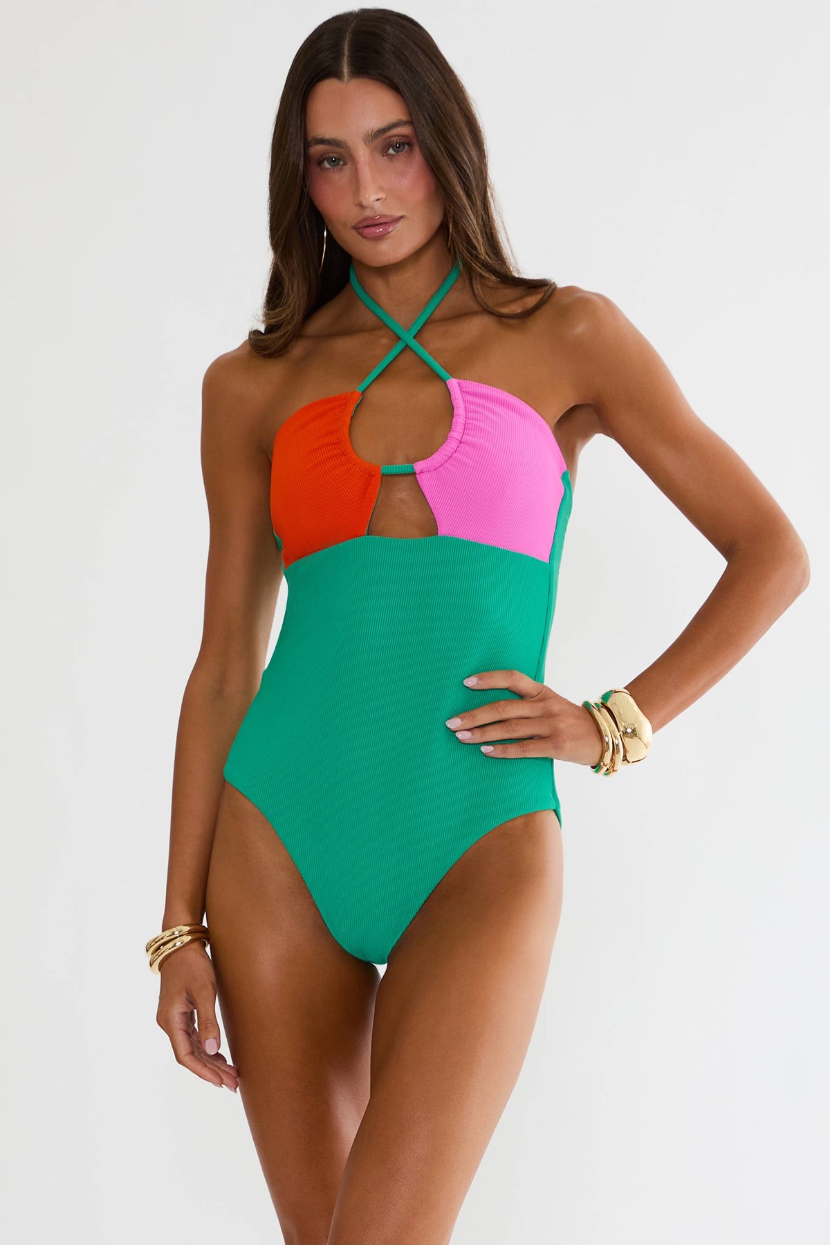 Woman wearing a colorblock criss cross halter one piece in front of a white wall. 