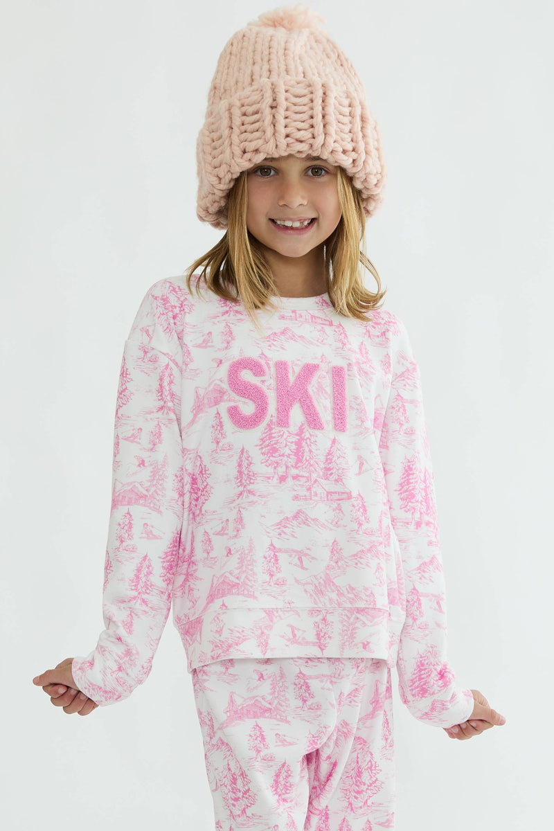 Child wearing a pink 'SKI' sweatshirt and matching pants with a white background