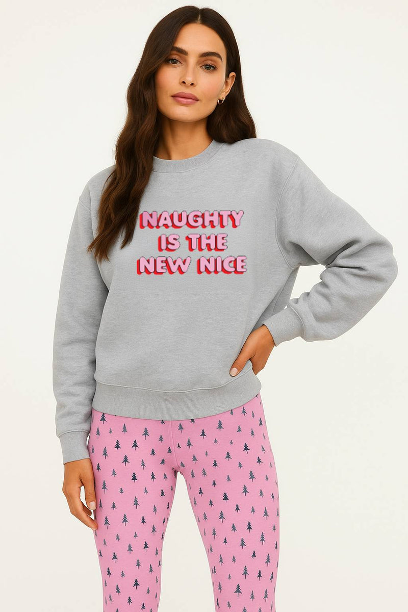 Woman wearing a gray sweatshirt with 'Naughty is the New Nice' text and pink pajama pants on a white background