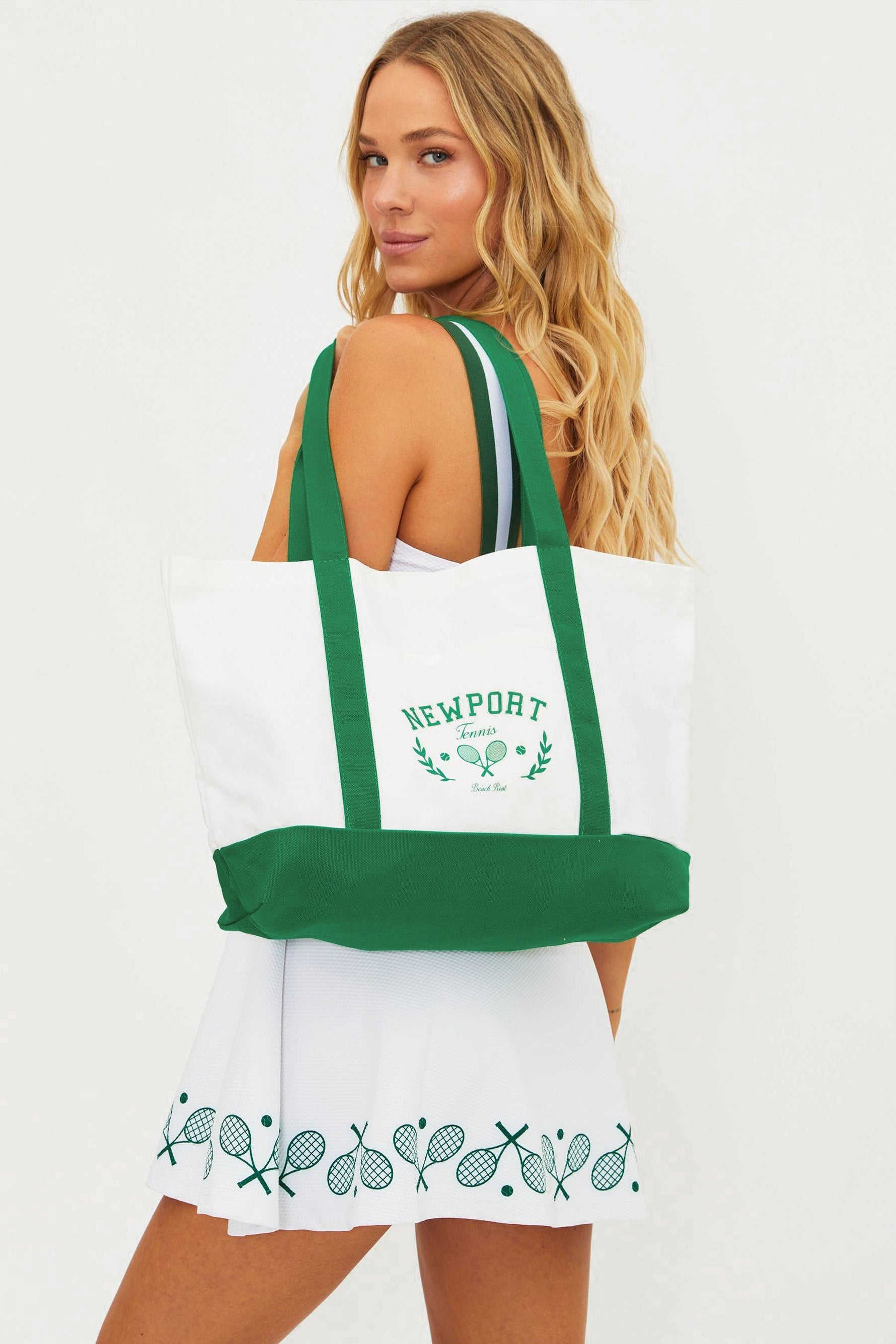 Woman holding a white tote bag with green straps and 'Newport' branding.