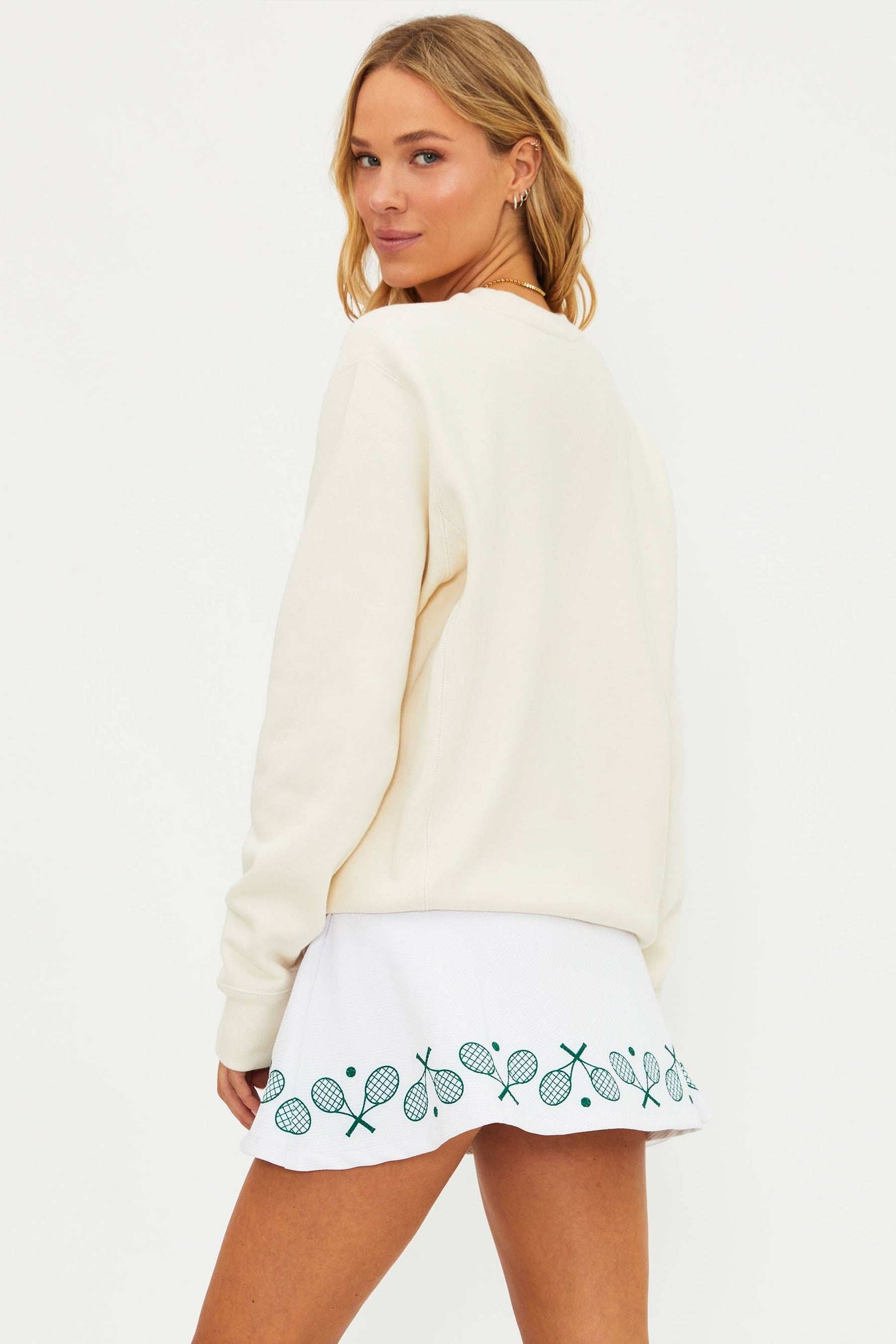 Woman wearing a white sweater and white skirt with embroidery on a plain background