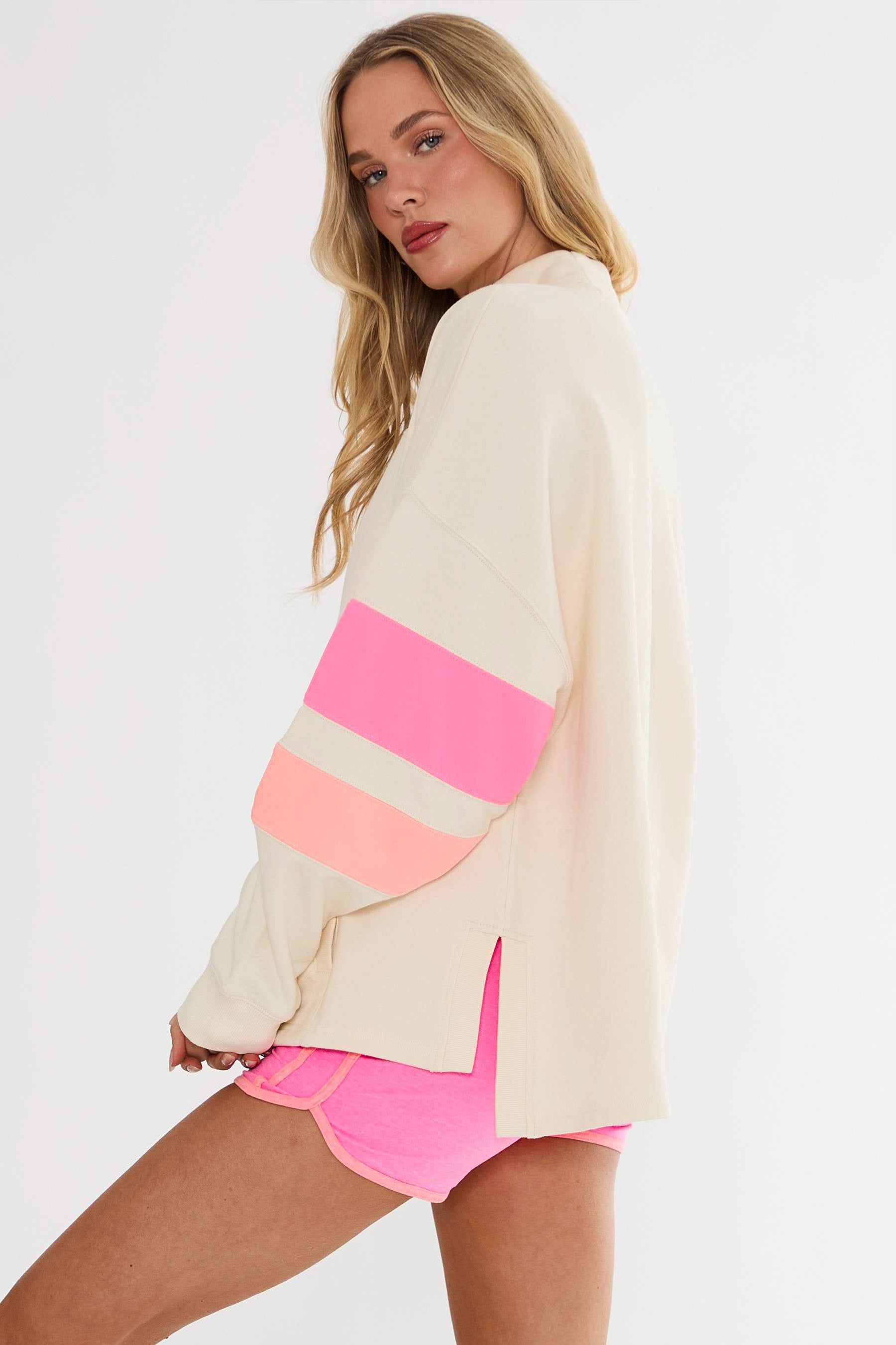 Woman wearing a cream cardigan with pink and orange stripes and pink shorts on a white background