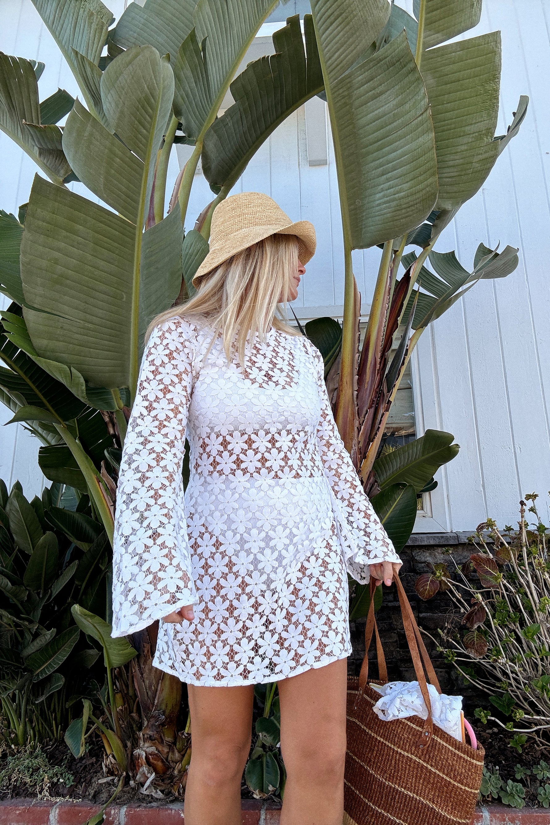 A white mini dress with floral lace detailing and three-quarter sleeves, worn by a model posing.