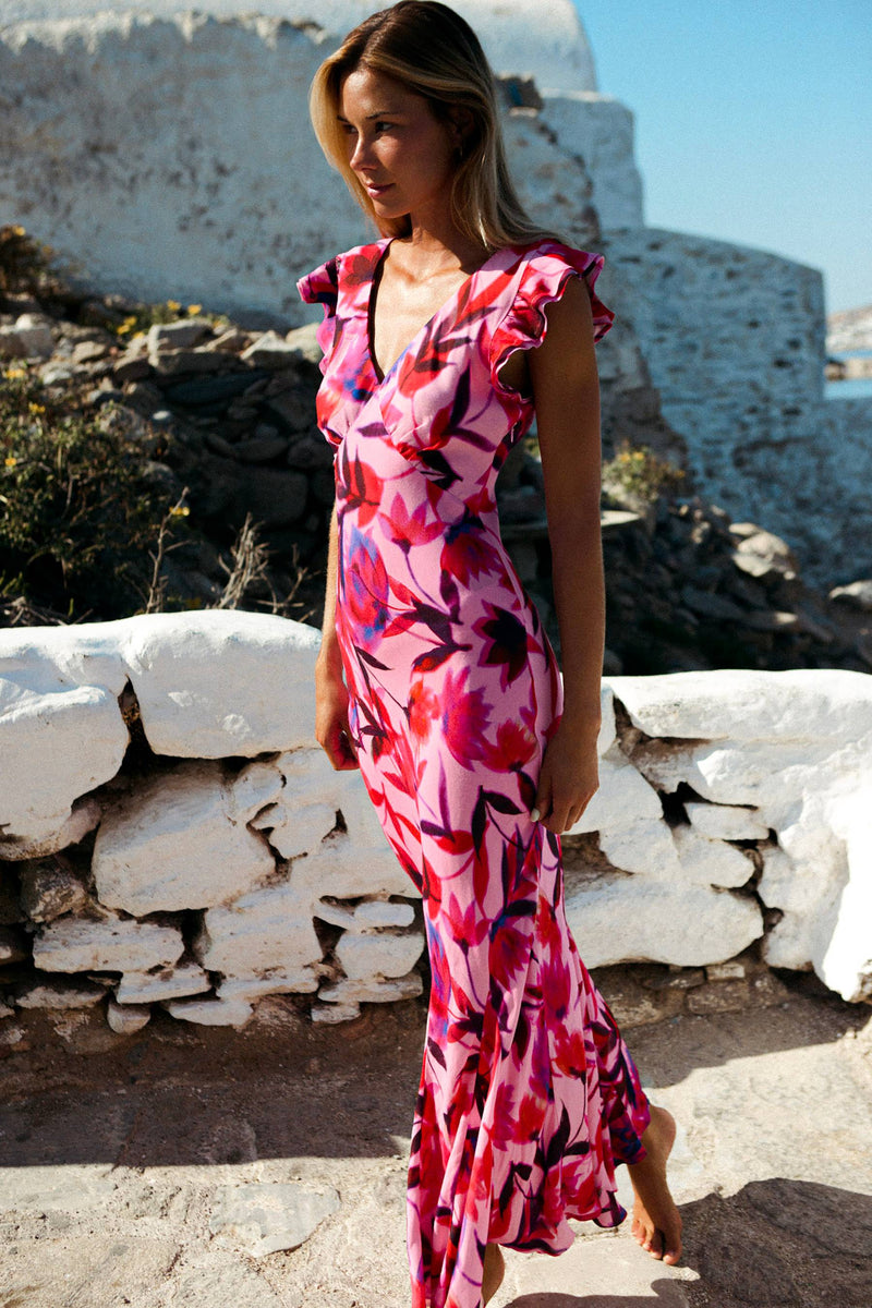 Woman wearing a vibrant maxi dress with hot pink, red, and black flowers. 