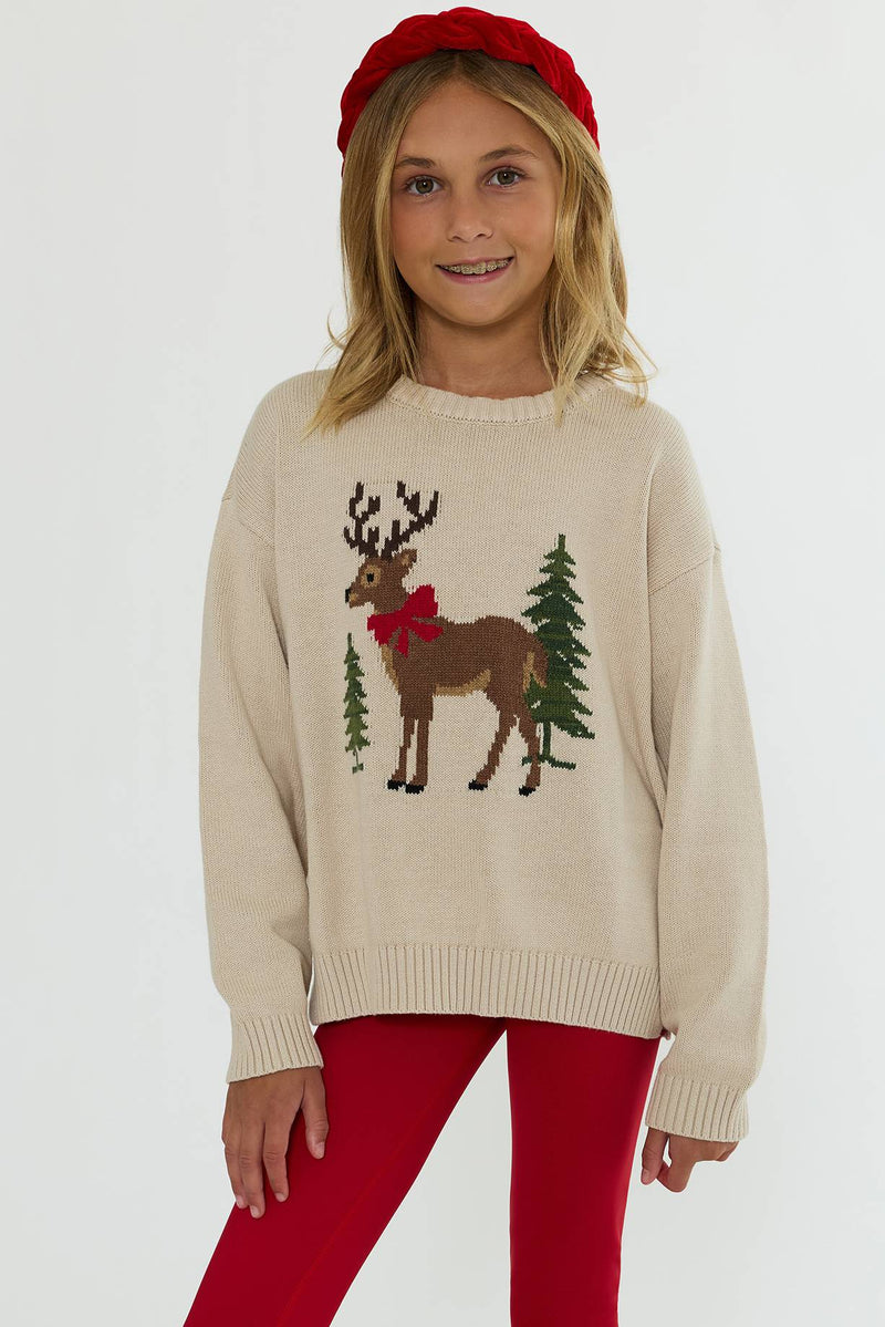 A young girl wearing a cream-colored knit sweater with a Christmas reindeer and pine tree design, paired with red leggings and a red beret, against a plain white background.