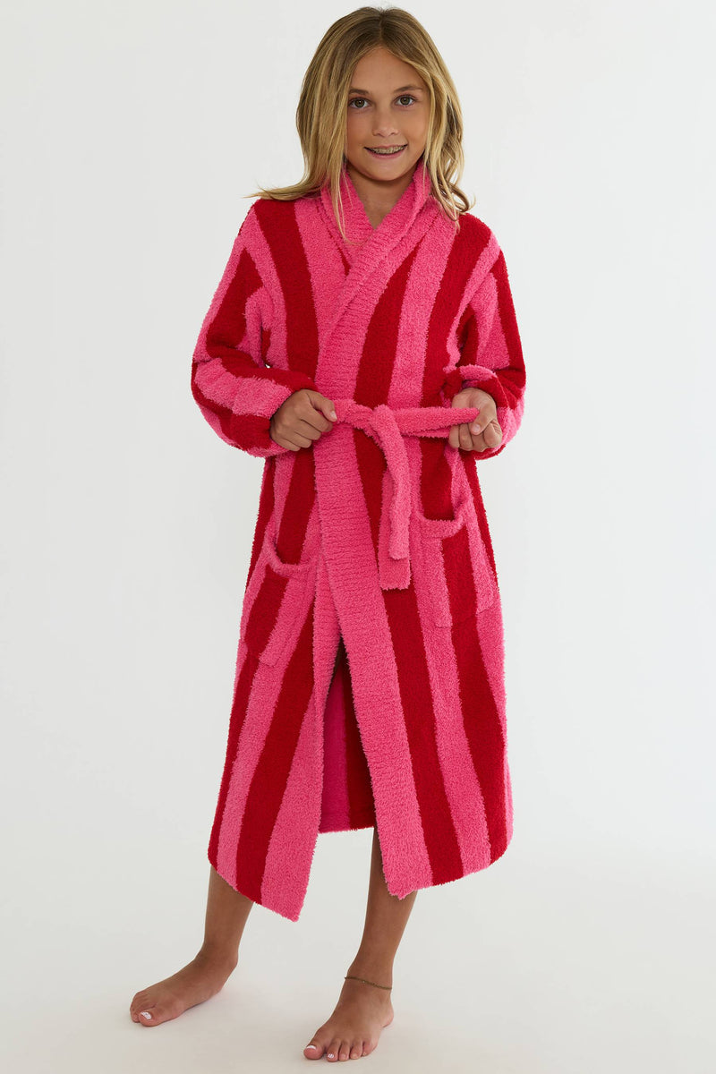 A young girl wearing a plush, long-sleeved bathrobe with vertical stripes in bright pink and deep red, standing against a plain white studio background.