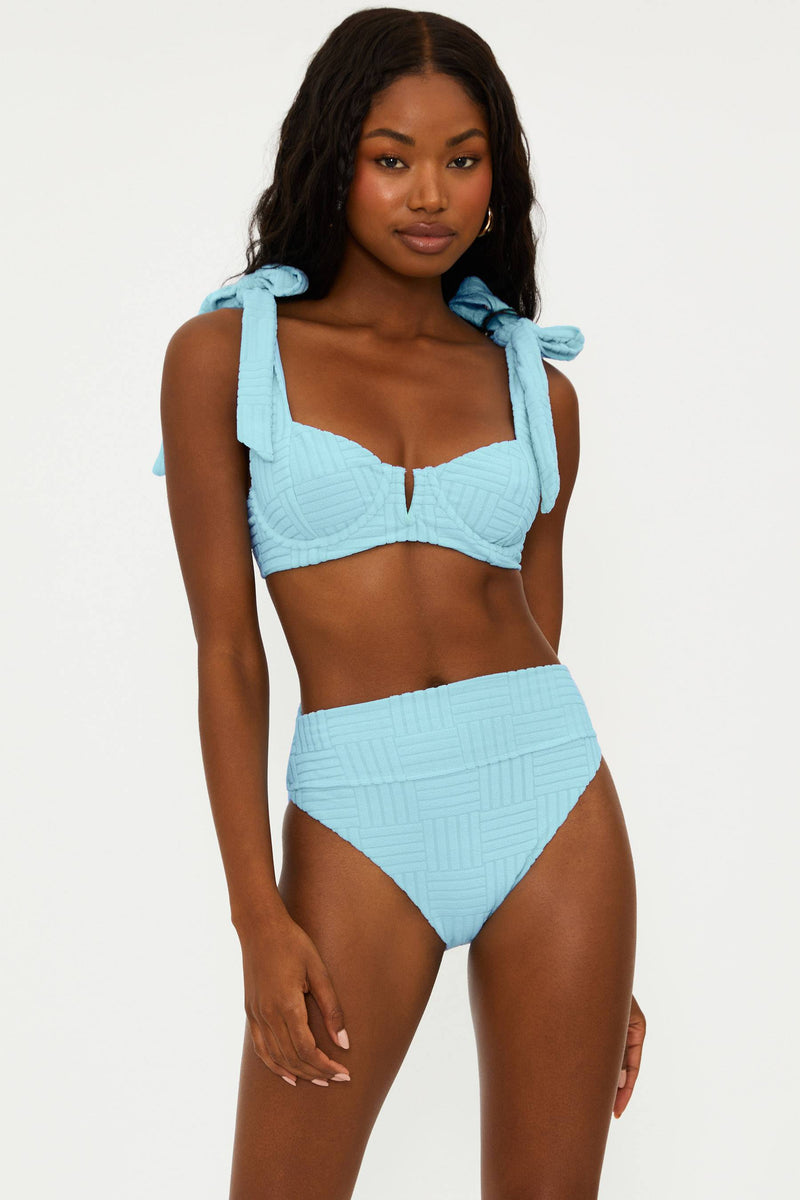 A woman wearing a blue bikini top with a sweetheart neckline and self-tie shoulders, made of terry fabric.
