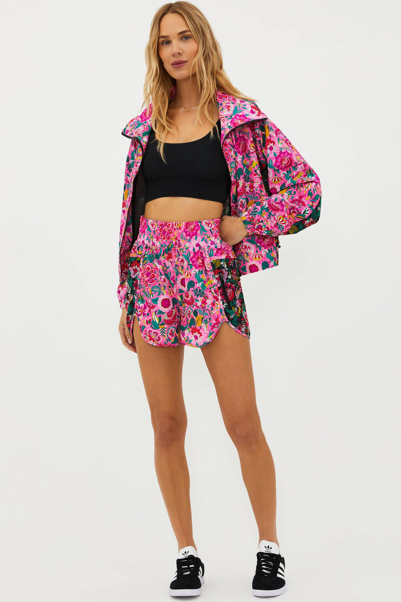 A model wearing vibrant passion floral running shorts with a wide elasticated waistband and a side zip pocket, paired with a black sports crop top.
