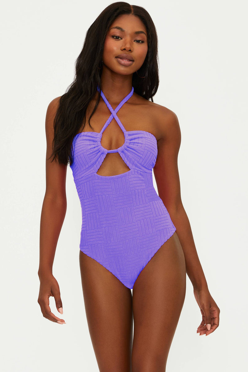 A model wearing a ultra violet terry one-piece swimsuit with an adjustable halter neck and cut out detail.