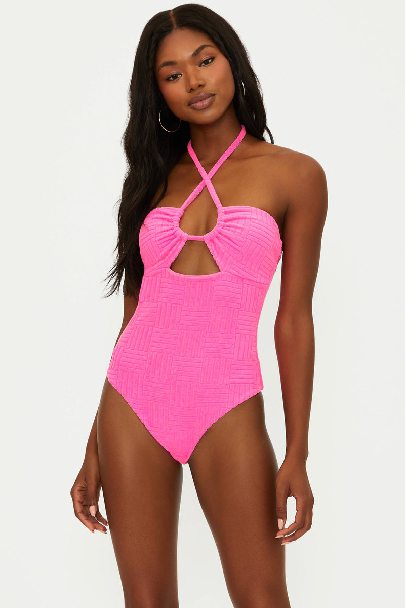 A model wearing a pink one-piece swimsuit with an adjustable halter neck and cut-out detail.