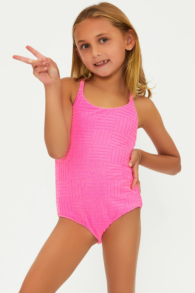 A young girl posing in a pink one-piece swimsuit with a textured pattern.