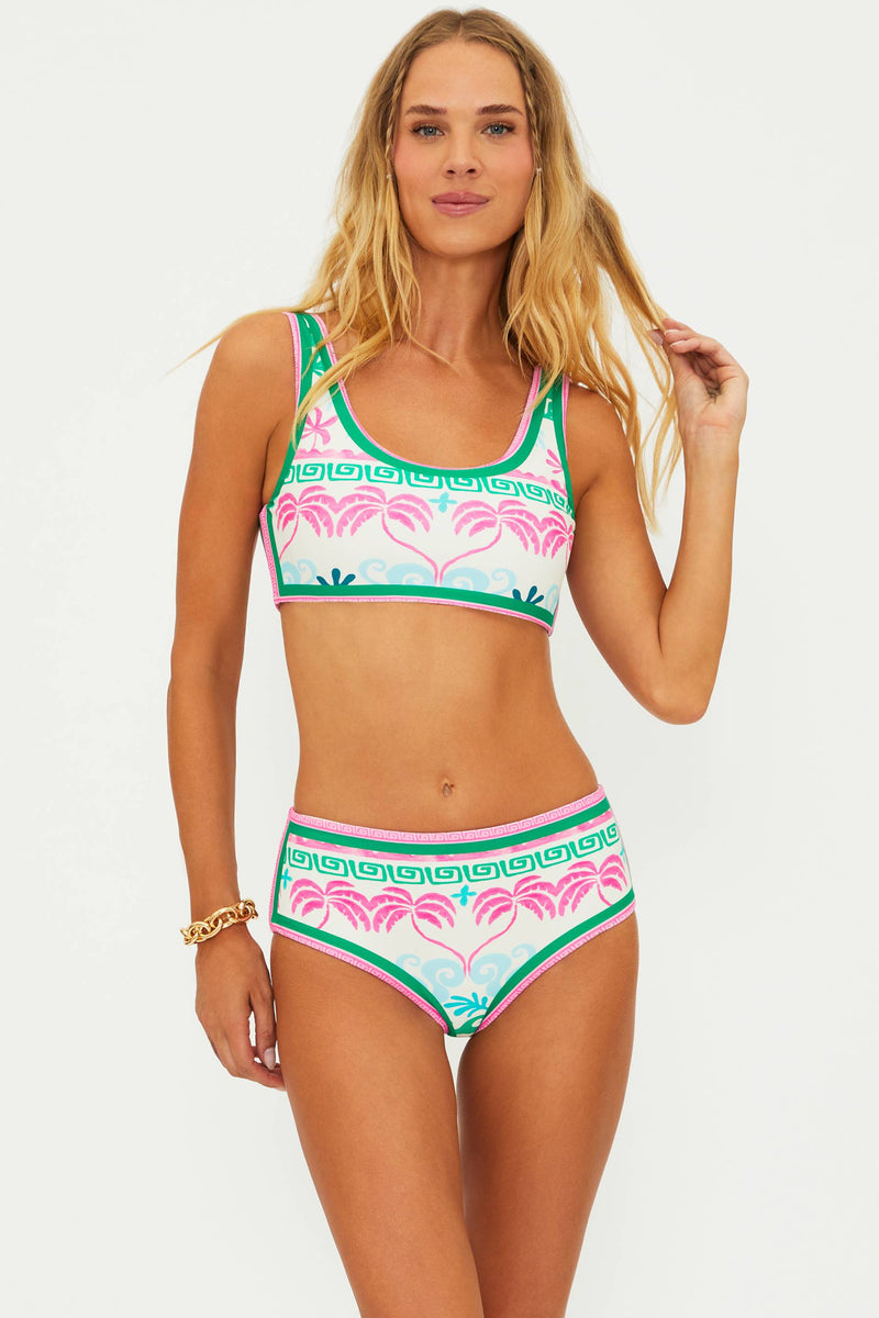 A woman wearing a tropical palm print swim top with a scoop neckline and fixed shoulder straps.