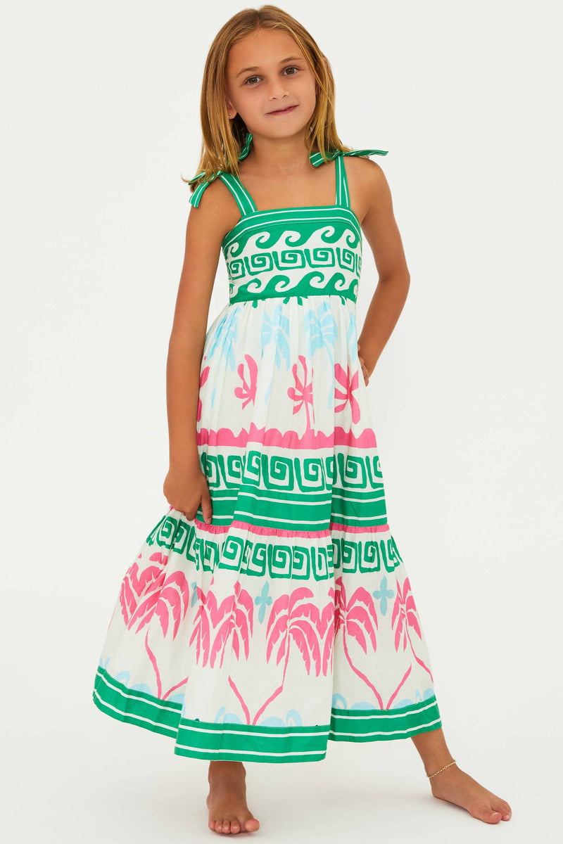 A girl wearing a sleeveless, squareneck, tropical palm print dress with tie straps and hand wash recommended label.