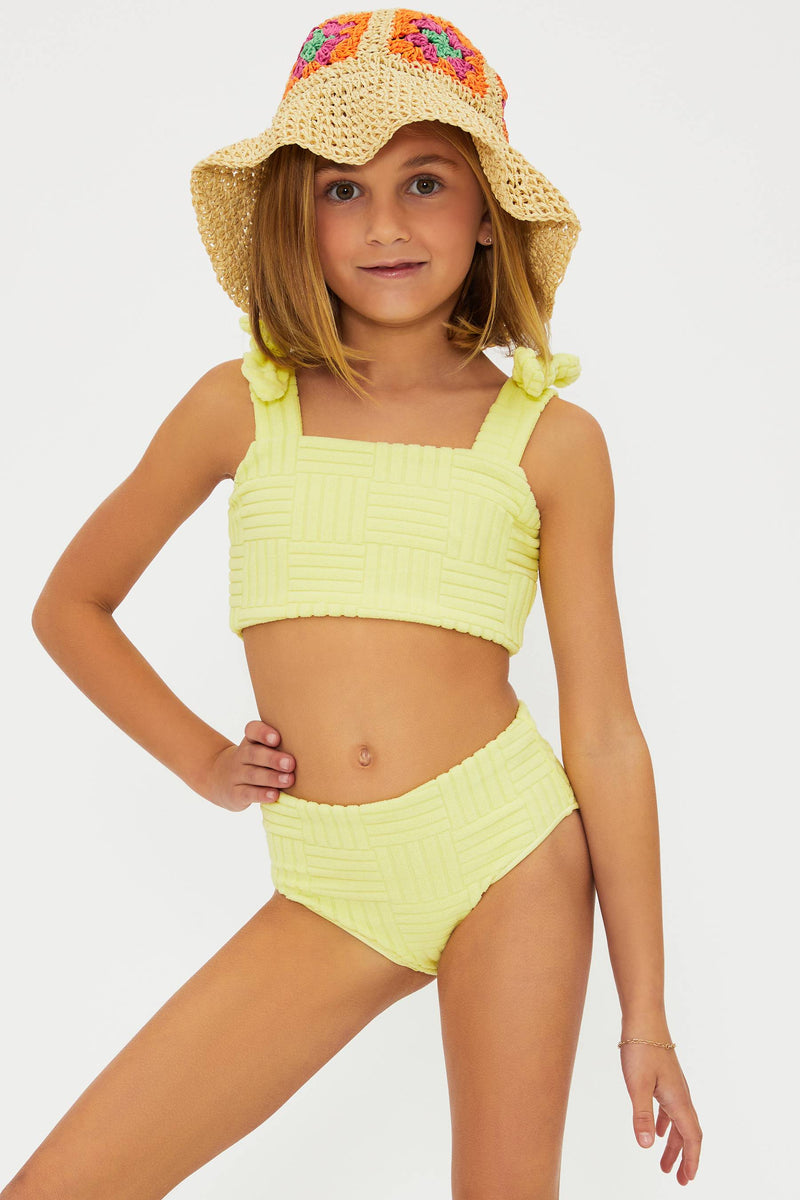 A young girl modeling a yellow high-waisted bikini bottom and a tankini top with bows on the shoulder straps, paired with a hat.