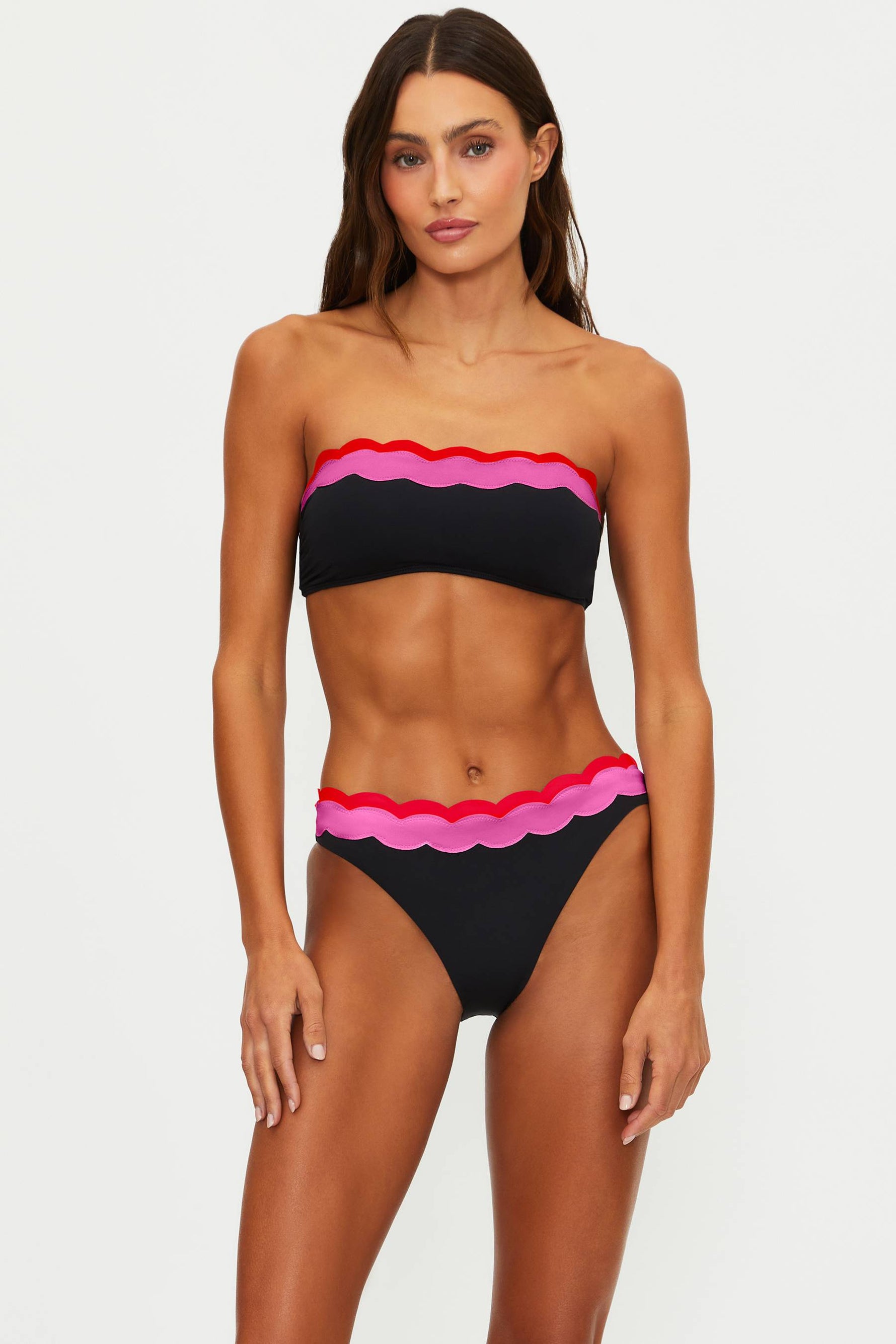 Woman wearing a black and pink bikini with scalloped edges on a white background