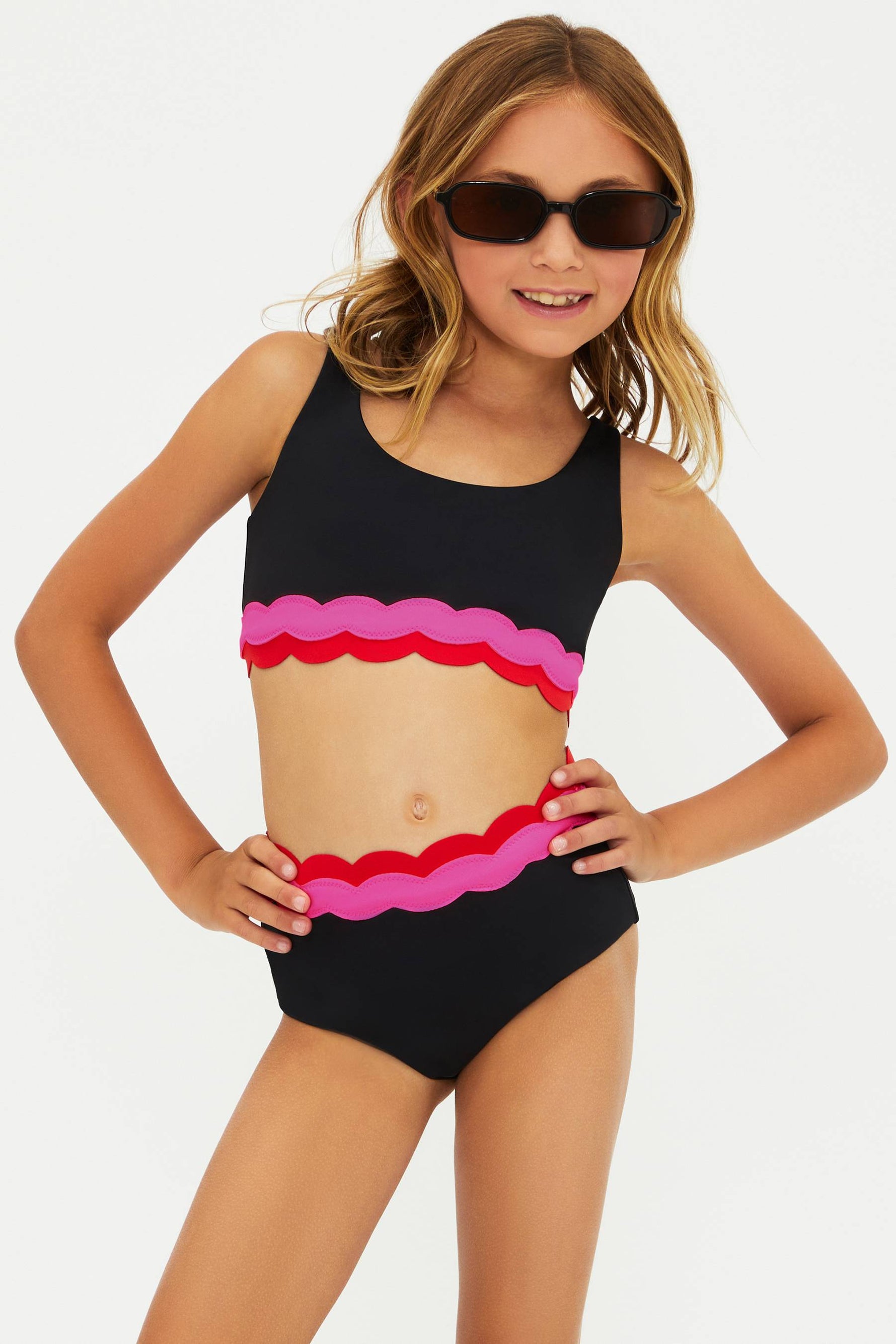 Young girl wearing a black swimsuit with pink ruffle design on a white background