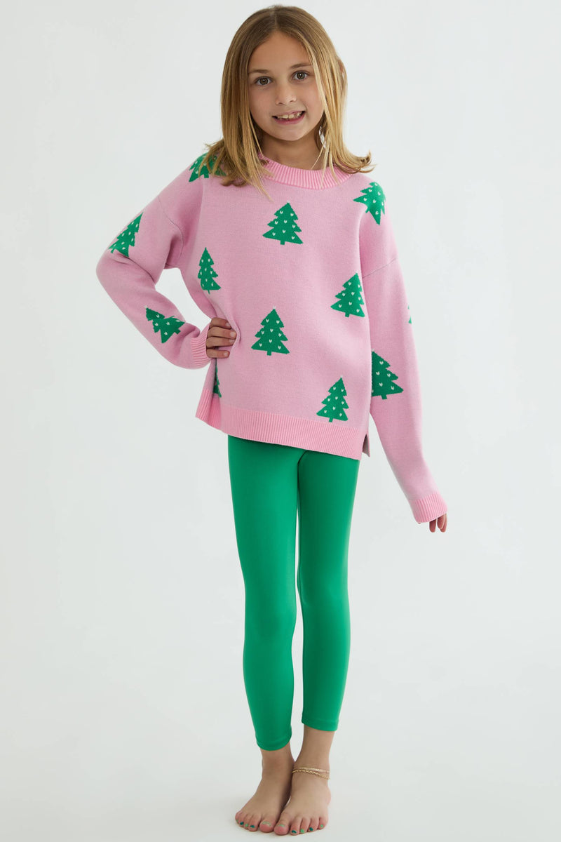 Young girl wearing a pink sweater with green tree patterns and green leggings on a white background