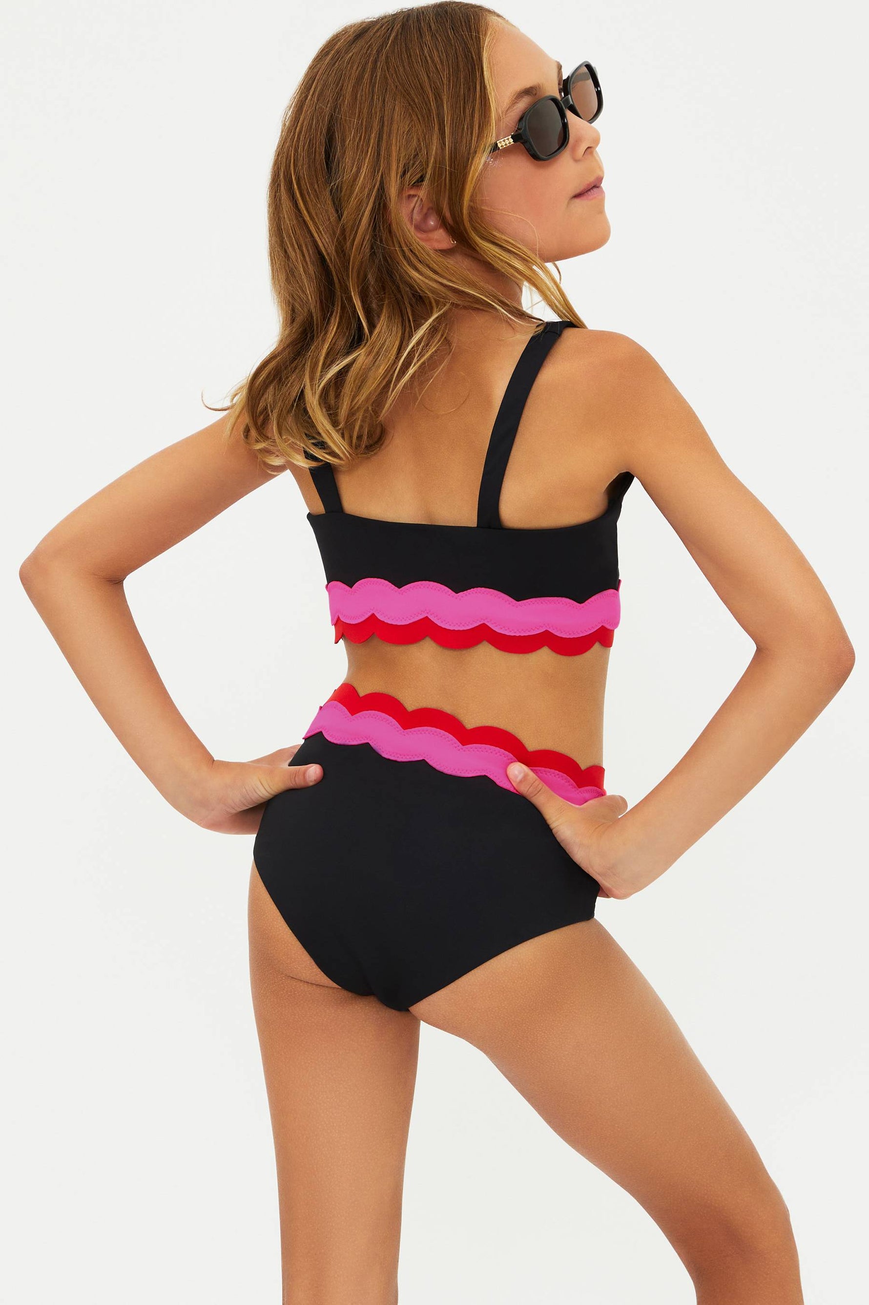 Woman wearing a black and pink swimsuit with sunglasses on a white background