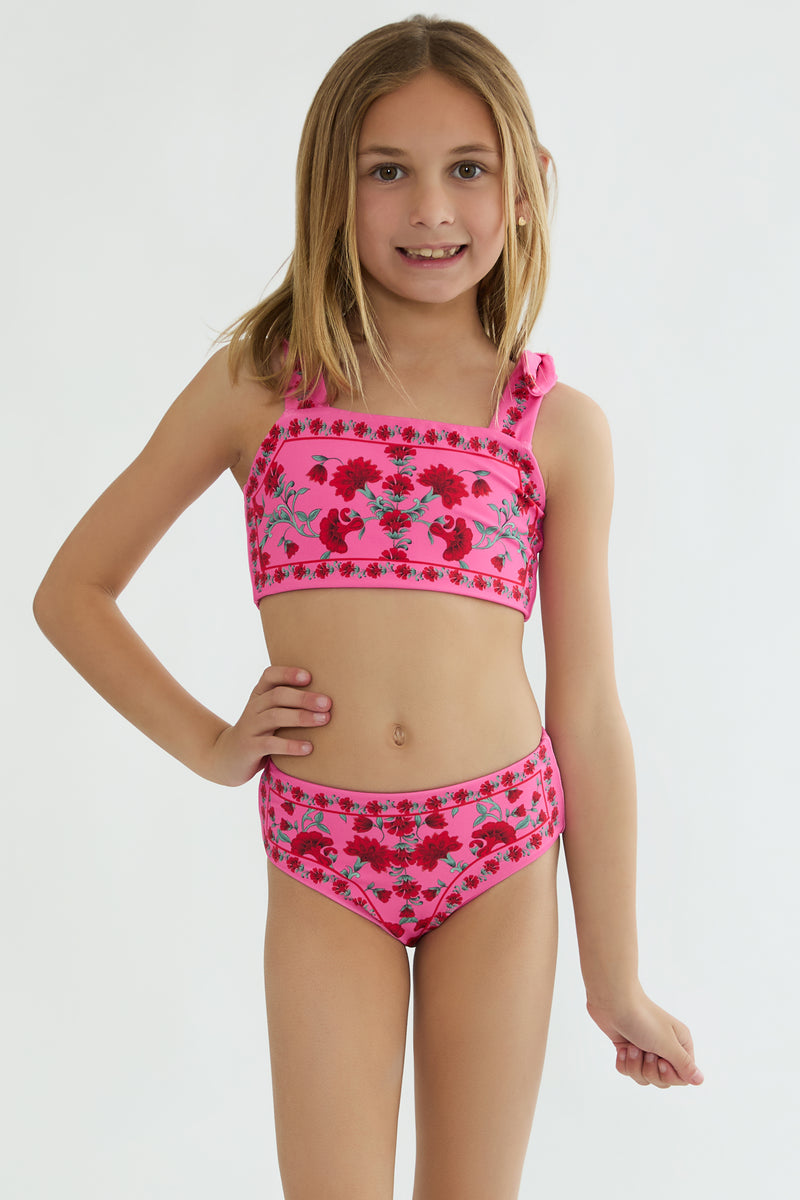 Young girl wearing a pink floral two-piece swimsuit on a white background