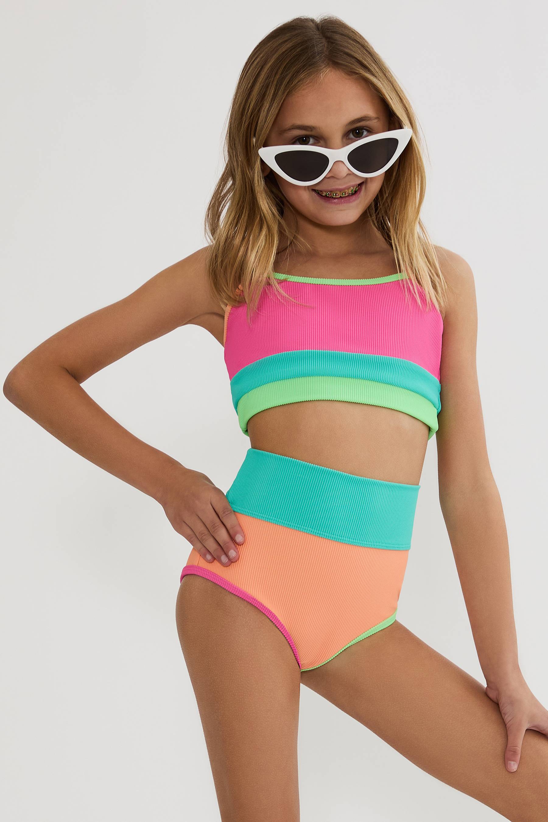 Young girl wearing a colorful two-piece swimsuit and sunglasses on a white background