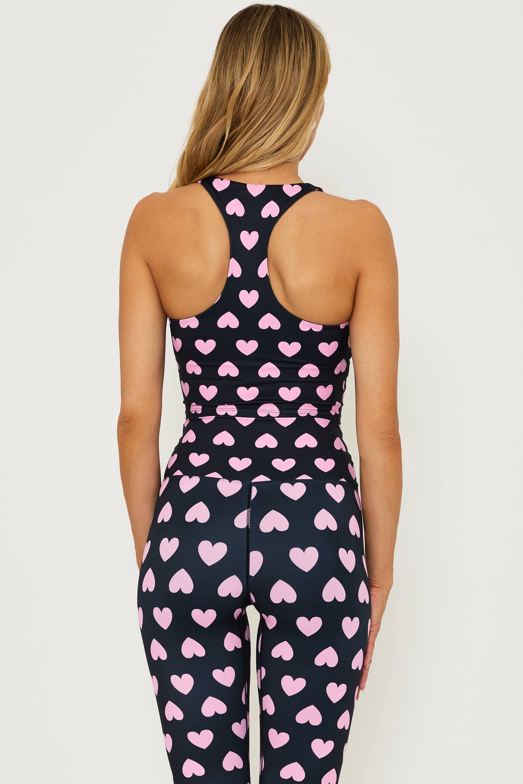 black full length high waisted leggings with pink hearts printed all over and a matching black crop top that is black with pink hearts