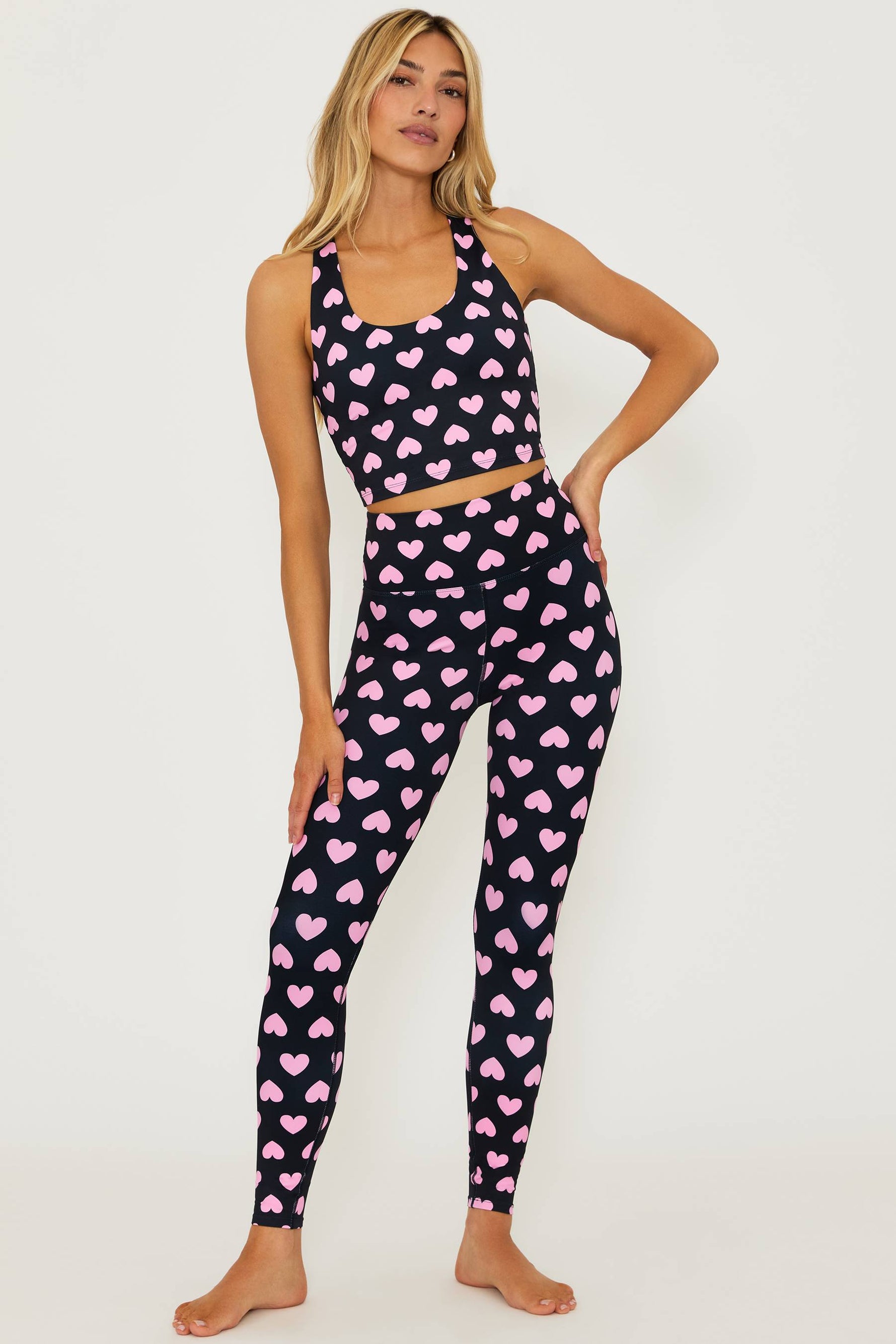 black full length high waisted leggings with pink hearts printed all over and a matching black crop top that is black with pink hearts