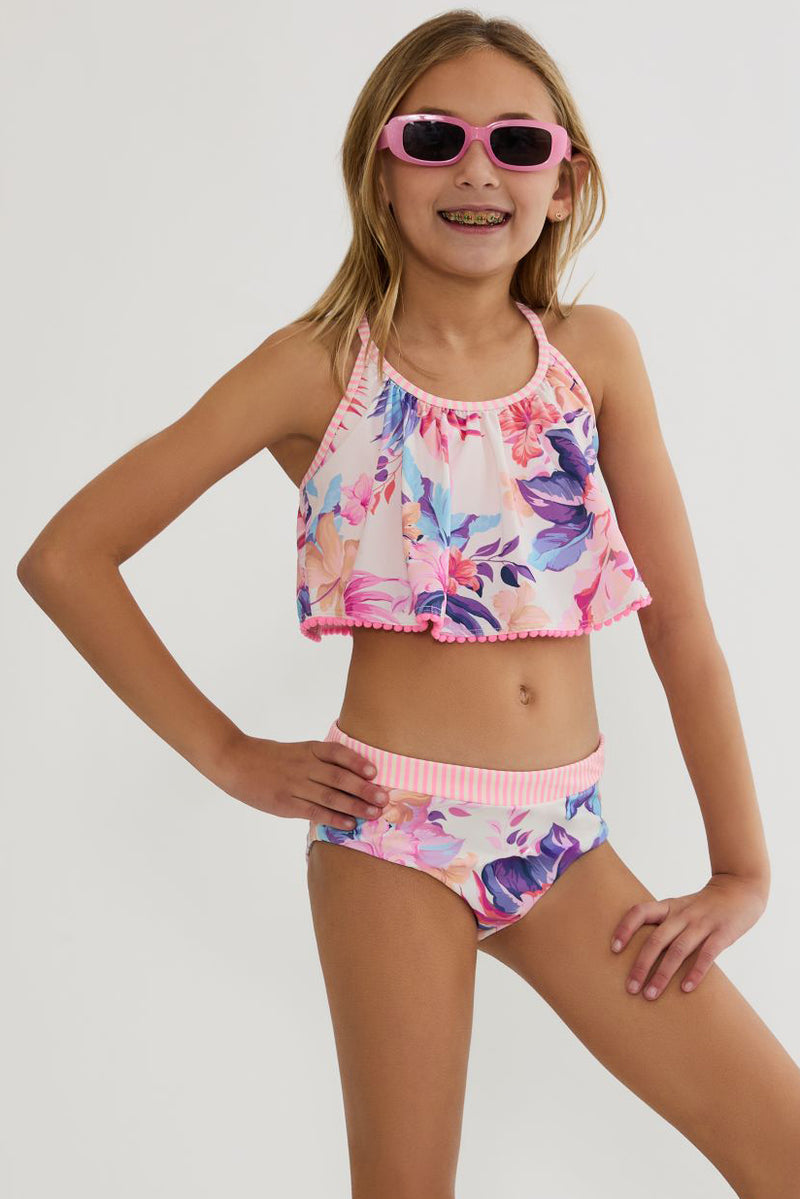 Young girl wearing a floral two-piece swimsuit and pink sunglasses on a white background