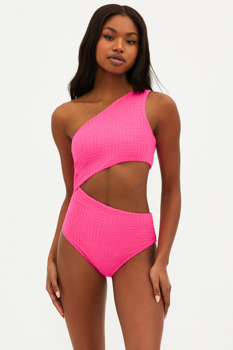 A model wearing a bright pink, asymmetrical one-piece swimsuit with side cutouts.